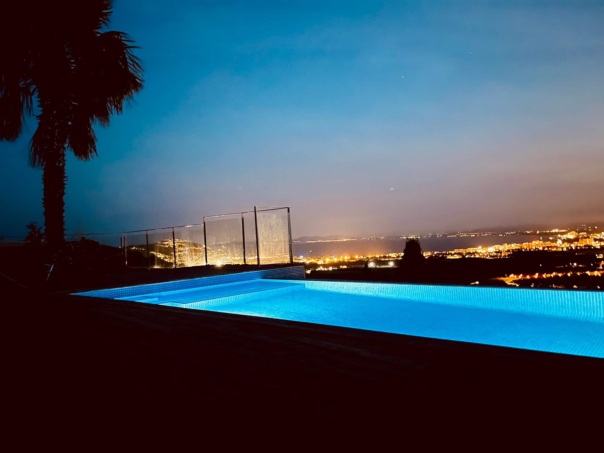 Pool lit blue at night with the city lights below