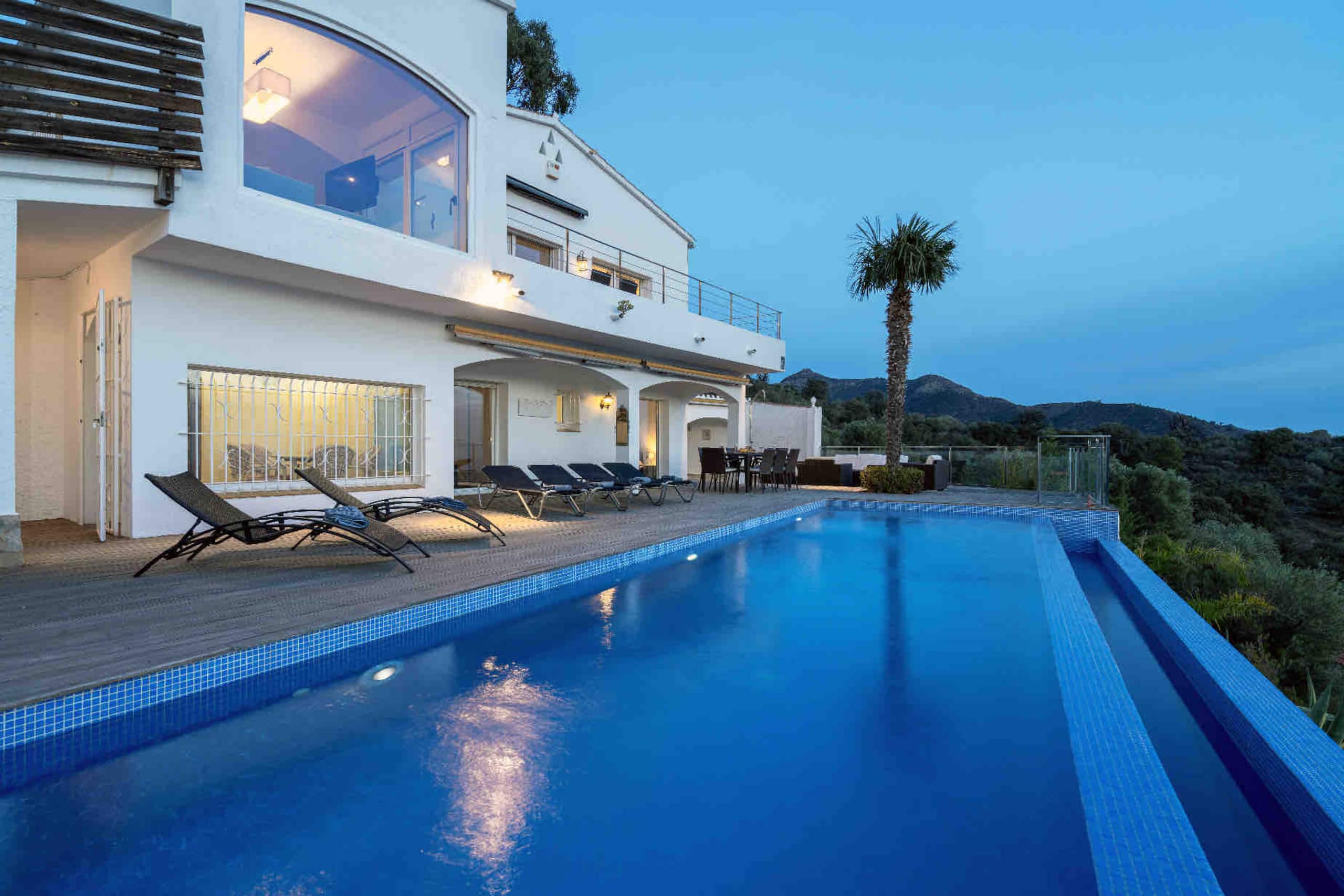 Lit infinity pool at dusk beside the villa terrace