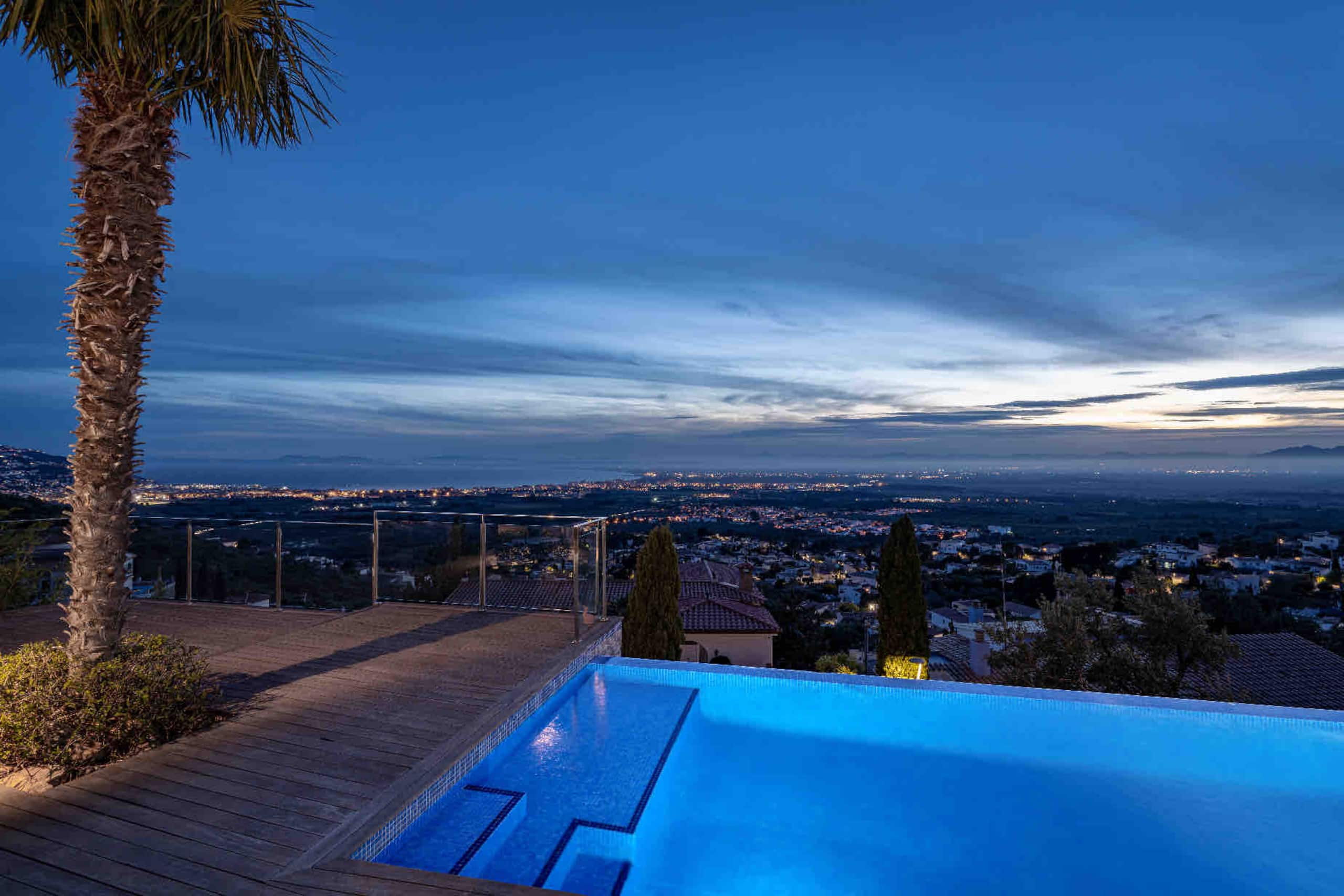 Night falls over the pool, palm tree and city lights below